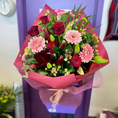 Ruby Romance Bouquet - A luxurious romantic bouquet of deep red roses, blush pink gerberas, red lilies and green button chrysanthemums, elegantly wrapped in burgundy paper and netting with an organza bow. The ultimate gift to say "I love you."