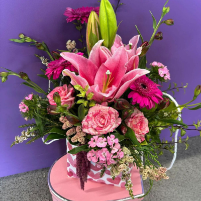 Pink Passion Lily Box - A romantic bloom box brimming with a statement pink Oriental lily, hot-pink gerberas, ruffled roses and delicate dianthus, all set in a heart-print gift bag. A sweet, girly gift for birthdays or "just because." Presented in a carry-style flower bag.